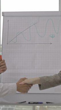 Kartvizitle beyaz tahtanın önünde el sıkışan erkek ve kadın.