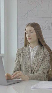 Genç bayan çalışan bir iş projesi üzerinde çalışıyor, modern bir iş yerinde dizüstü bilgisayarıyla yazı yazıyor.