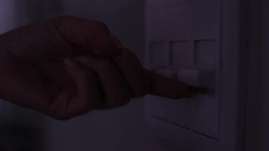 Beyaz ışık düğmesini açan bir kadının eli, odayı karanlıktan aydınlığa aydınlatıyor.