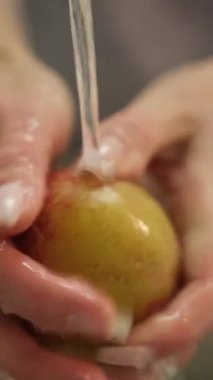 Dişi eller akarsu deresinin altında taze kırmızı ve sarı bir elmayı dikkatlice yıkıyor.