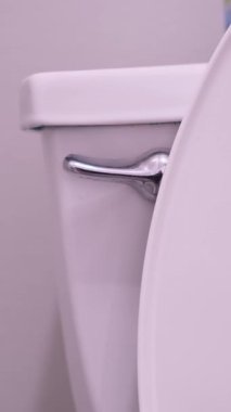 Banyoda beyaz bir tuvaletin sifonunu çeken birinin yakın plan görüntüsü.