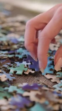 Manikürlü bir kadın, ahşap bir masadaki renkli yapboz parçalarını arıyor.