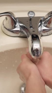 Banyoda musluk suyunun altında ellerini yıkayan birinin yakın çekimi.