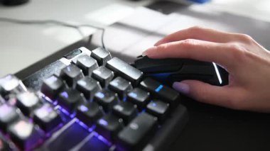 Renkli mekanik klavyenin yanında oyun faresi kullanan bir kadının yakın plan fotoğrafı.