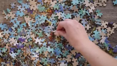 Tahta bir masanın üzerindeki renkli yapboz parçalarını ayıran bir elin yukarıdan aşağı görüntüsü
