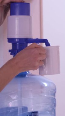 İnsanlar, ofisteki beyaz bardağa büyük bir şişeden temiz su pompalıyorlar.