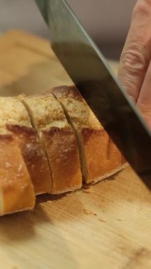 Tahta kesme tahtasına mutfak bıçağıyla taze ekmek kesen birinin yakın çekimi.