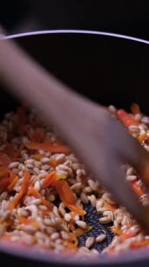 Koyu bir tencerede ahşap kaşıkla karıştırılan havuçla inci arpası pişirme