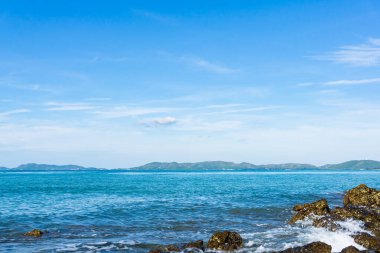 Mavi denizdeki kayalar. Aşağıya baktığınızda, uzun bir ada sırası görebiliyordunuz, ve arka planda gökyüzü ve beyaz kabarık bulutlar vardı. Yaz tatili atmosferi