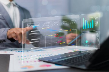 Bir masanın üzerine yerleştirilmiş sanal grafik ve belgeleri analiz ederek ilerlemeyi izlemek için bir program planlama ve çalıştırma idari konsepti. Dizüstü bilgisayarı olan bir iş adamı.
