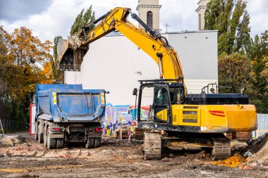 Kazıcı, güpegündüz inşaat alanında bir çöp kamyonuna toprak yüklüyor..