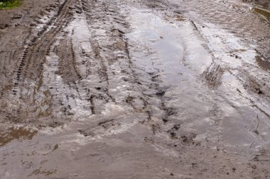Çamurlu toprakta lastik izleri, ayak izleri ve araç izleri var. Açık hava, nemli toprak ve desenli doğal doku..