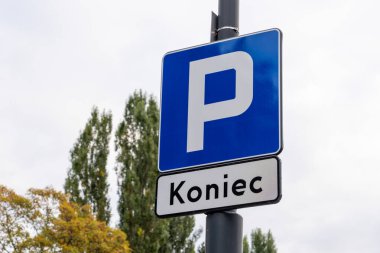 Bir şehir caddesindeki park alanının sonunu gösteren bir Koniec alt işareti olan park levhası, yerel trafik yönetmeliklerini gösteriyor.