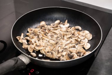 Dilimlenmiş şampiyon mantarları kızartma tavasında cızırdıyor, buhar salıyor ve sıcak bir mutfakta yemek pişirirken altın rengine dönüyor..