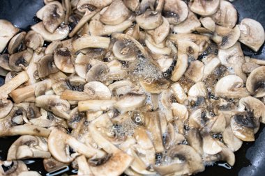 Dilimlenmiş şampiyon mantarları kızartma tavasında cızırdıyor, buhar salıyor ve sıcak bir mutfakta yemek pişirirken altın rengine dönüyor..