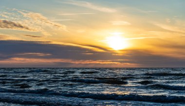 Yumuşak dalgalar ve suda parlayan yansımalarla denizin üzerinde altın gün batımı. Sıcak akşam ışığı ile huzurlu deniz manzarası.