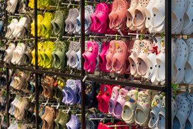 Bir timsah dükkanının içinde canlı, renkli timsah ayakkabılarından oluşan bir duvar görüntüle, müşteriler için çeşitli stil ve renkler sergilenir.