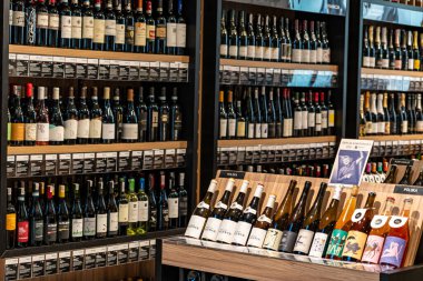 Güzel düzenlenmiş şişeler, ahşap raflar ve şarap tatma ve alışveriş meraklıları için sıcak bir atmosfer sunan rahat bir şarap dükkanı.