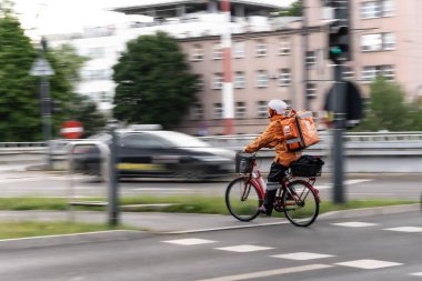 Bisikletli kurye sırtında bir sırt çantasıyla şehir caddesinden geçiyor..
