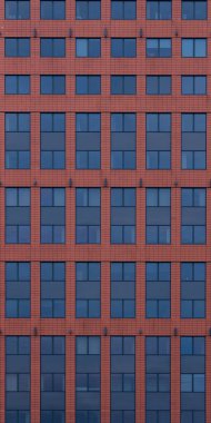 Koyu mavi camlı düz kırmızı tuğla bir duvar, simetrik olarak sıralanmış ve doğal gün ışığında fotoğraflanmış..