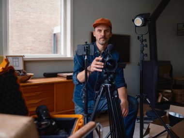 Film yapımcısı video kamera donanımını modern ev stüdyo ortamında doğrudan izleyiciye sunar.