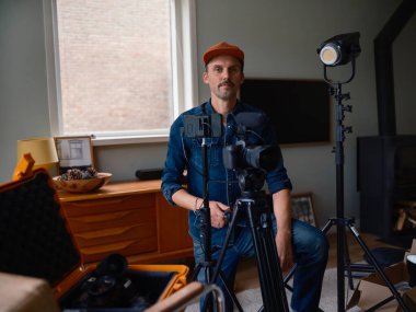 Günümüz ev yapımı stüdyosunda profesyonel kamera teçhizatının yanında duran kendinden emin film yapımcısı.