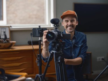 Kameraman, ev stüdyosunda kendine güveni olan kamera ekipmanlarını izleyiciye sunuyor.