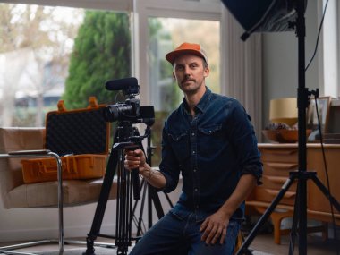 Profesyonel film yapımcısı kamerayla otururken stüdyo ortamında kendine güveni gösteriyor.