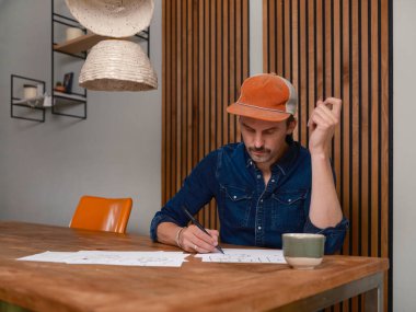 Film yapımcısı özenle ahşap çalışma masasında maket kağıtları ve kahve fincanıyla duruyor.