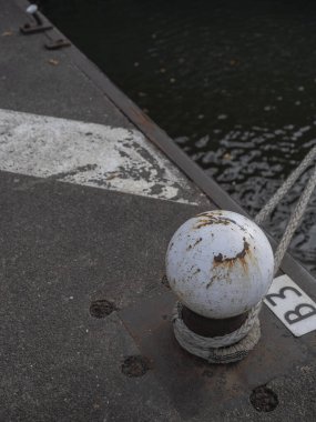 Su yüzeyi olan beton rıhtımda halatı emniyete alan yıpranmış beyaz boğa yakından görülüyor.