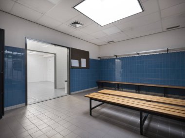 Spor salonunun soyunma odasının açılı görünümü dolapları ve karakteristik mavi fayanslı mimari tasarımı gösteriyor