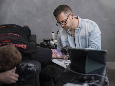 Dövmeci kırmızı sırt çantası ve teçhizatla müşteri kolu üzerinde çalışıyor