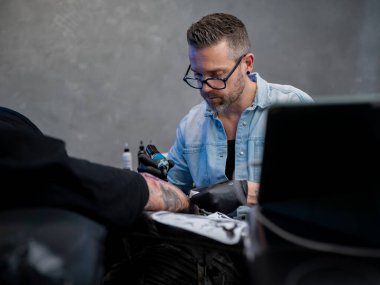 Stüdyo ortamında müşteriler üzerinde çalışan konsantre erkek dövme sanatçısının portresi