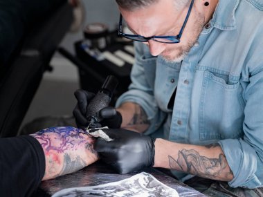 Dövme sanatçısının kolunda görünür mor şablonlu renkli Japon peyzaj tasarımı üzerine yoğunlaşmış çalışmasının yakın plan görüntüsü.