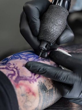 Dövme makinesinin yakın çekimi önkolunda görünür mor ve pembe şablon tasarımı olan renkli Japon manzarasına mürekkep uyguluyor..