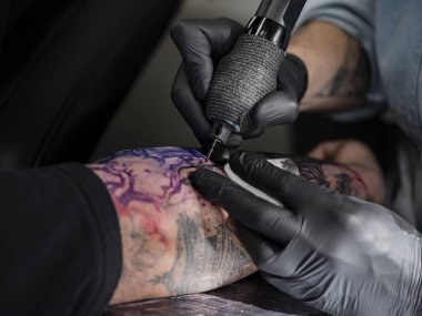 Renkli Japon peyzaj tasarımına yerleştirilmiş dövme makinesinin yakın plan resmi. Mor ve pembe renkleri tam iğne desenli..