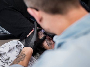 Dövme sanatçısının ellerinin yakın perspektifi cilt ve mürekkebe özen gösteren renkli Japon tasarımı üzerinde çalışıyor..