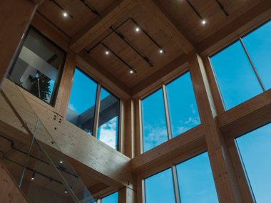 İç mimari geniş pencereli kereste kiriş tavan yapısını ve tepenin üzerindeki ışıklandırmayı gösteriyor.