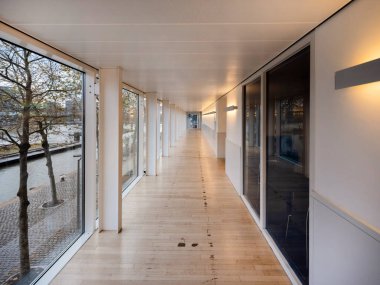 Geniş pencereleri ve doğal ışığı olan modern koridor sıcak iç atmosfer yaratıyor..