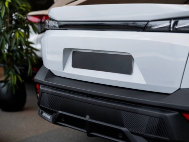 Beyaz aracın arka tampon kısmının siyah alt paneli ve arka lambası görünür.