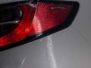 Dramatik otomotiv aydınlatma ve kontrastlı su damlacıkları içeren ıslak kırmızı arka lambaların yakın çekimi