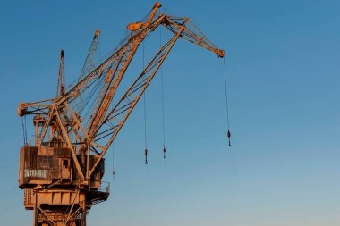 Açık mavi gökyüzüne karşı kanca ve kabloyla yıpranmış turuncu liman vinci.