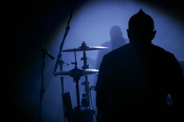 Davul setindeki siluetli davulcu dramatik mavi tiyatro ışıklandırmasıyla sahnede performans sergiliyor