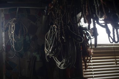 Denizcilik atölyesinde pencere ışığıyla sarmalanmış halatlar ve denizcilik ekipmanları asılı.