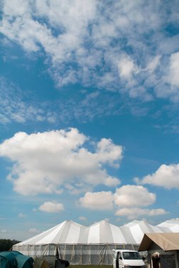 Mavi gökyüzüne karşı büyük beyaz ve bej çizgili sirk tarzı bir çadır. Festival ve açık hava toplantıları ve eğlence mekanı.
