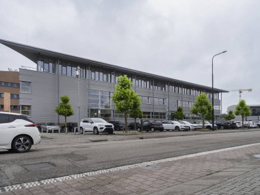 Bulutlu bir günde cadde seviyesinden manzaralı metal cepheli ve otoparklı modern üç katlı ofis binası.