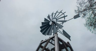 Sanayi tasarımı ve yenilenebilir enerji sembolizmini gösteren bulutlu gökyüzüne karşı modern metal yel değirmeni yapısı