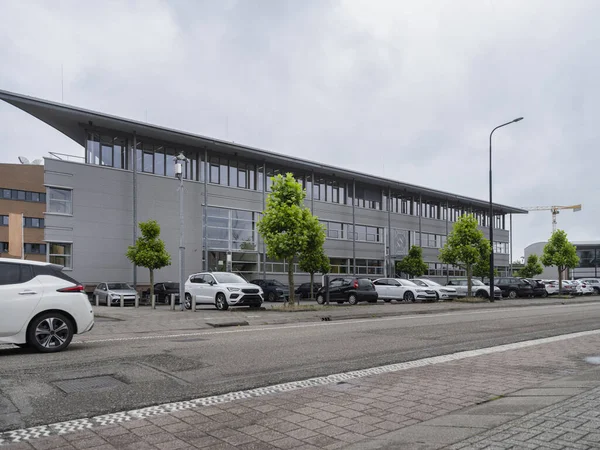 Bulutlu bir günde cadde seviyesinden manzaralı metal cepheli ve otoparklı modern üç katlı ofis binası.