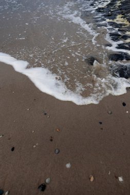 Kumlu sahilde çakıl taşlarıyla yıkanan okyanus dalgası köpüğü. Deniz ve doğa kavramları için kıyı su dokusu arka planı.