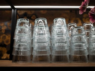 Barın rafında baş aşağı duran tırtıklı içki bardakları, çiçekli duvar kağıdı arka planı, konukseverlik iç mimarisi.